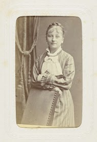 Studioportret van een vrouw in een lange jurk achter een stoel.