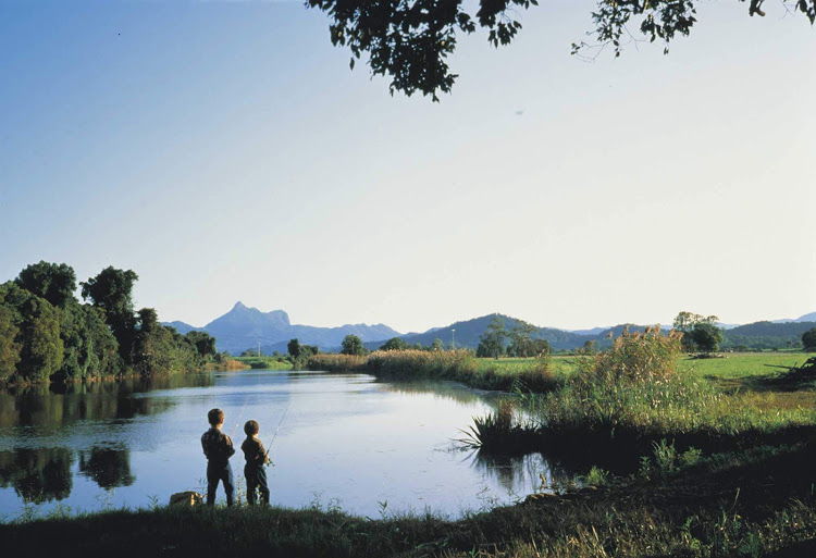 Boys fish on the Tweed River as the peak of Mount Warning looms above them in Australia.