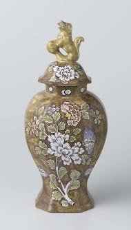 dekselpot van faience met op bruin fond een veelkleurige beschildering met bloemen. Op deksel een leeuw met bal