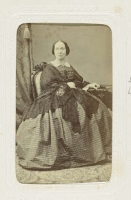 Studioportret van een vrouw in een bolle jurk, zij zit aan een dressoir