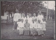 Groepsportret van mannen, vrouwen en kinderen voor een gebouw, vermoedelijk op het terrein van een ziekenhuis in Nederlands-Indië