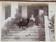 Vrouw en kind zittend op de trap van een huis, met twee honden