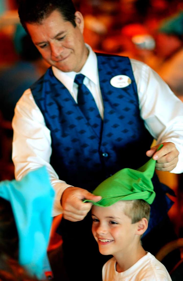 A boy gets fitted for a Robin Hood cap by a server during lunch on Disney Dream. 