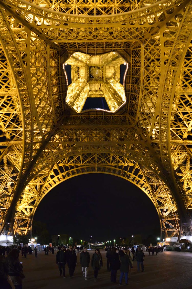 A view of the base of the Eiffel Tower in Paris at night. 