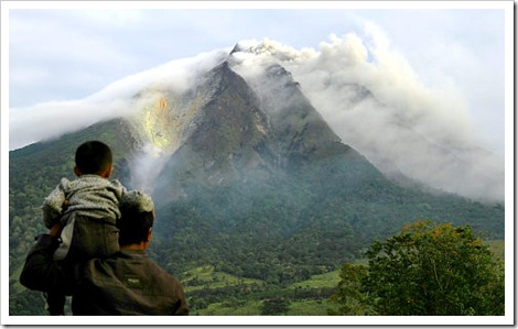 A man and his son look as the Sinabung volcano spews thick smoke in Karo district in North Sumatra