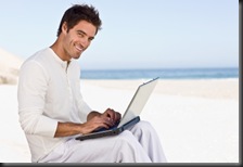 Happy young man using laptop on beach