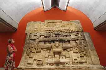 Curator Jennifer Casler Price stands in front of a cast of a temple facade that depicts a god of rain and lightning, top, and a god of lakes, rivers and oceans, center.