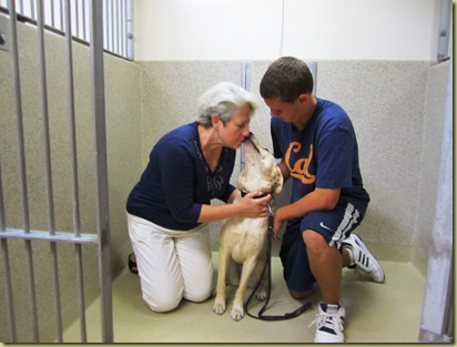 Judi and James in the kennel with Reyna.  Reyna is giving Judi a kiss on her face.