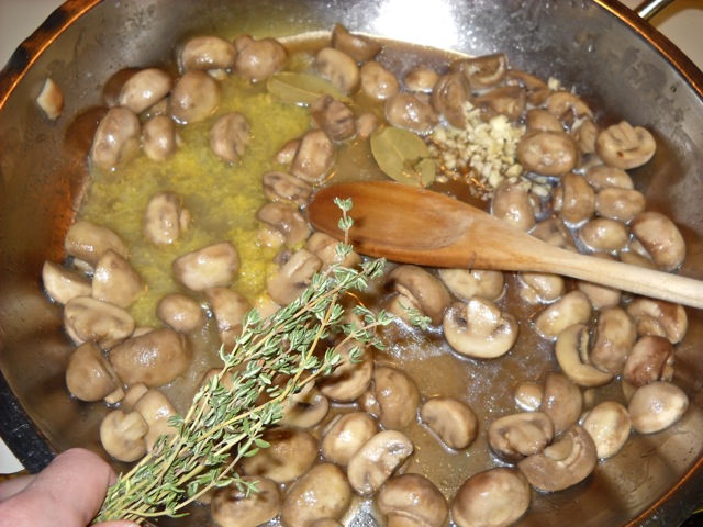 cooked mushrooms in pan, with seasoning of lemon juice, zest, garlic, bay leaf, thyme, olive oil, salt and pepper