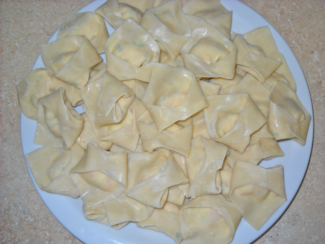 folded wontons on white plate ready to be cooked 