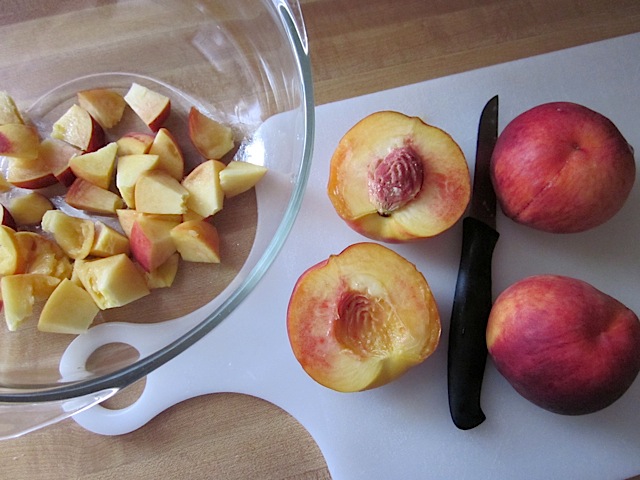 Dicing peaches with knife on cutting board, bowl of diced peaches on the side 
