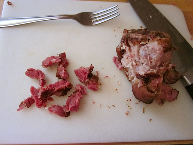 ham hock on cutting board with fork and knife being shredded 