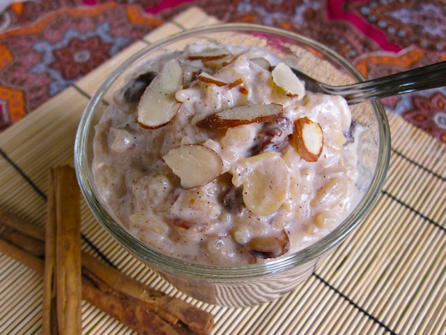 Rice Pudding in clear bowl, topped with sliced almonds and cinnamon sticks on the side 