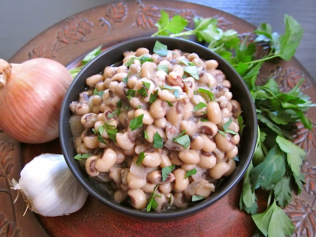 Black-eyed peas in black bowl with garlic, onion and cilantro staged on the side