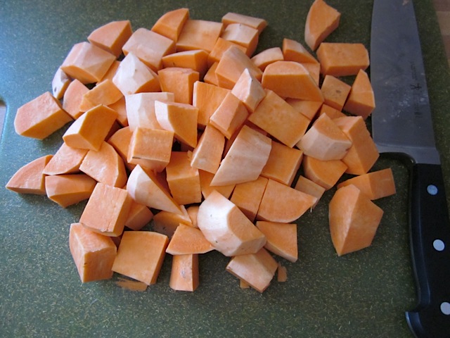 sweet potato cut into cubes with knife on cutting board 
