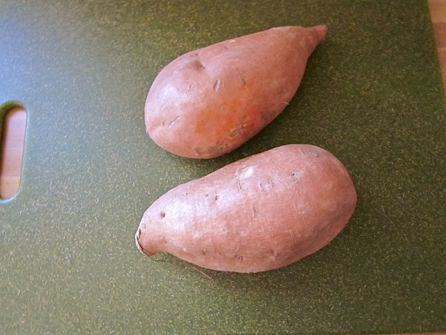 Two uncooked sweet potatoes on cutting board 