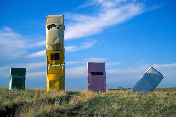 Five cars jut out of the ground at Carhenge, near Alliance, Nebraska, USA, 2004.

Carhenge is a replica of England's Stonehenge located near the city of Alliance, Nebraska on the High Plains. Instead of being made from stones, Carhenge is constructed of vintage American automobiles, all covered with gray spray paint. Built by Jim Reinders, it was dedicated at the June 1987 summer solstice. During the summer of 2006, a visitors' center was being constructed to service the site.  Thirty-eight automobiles were used in a circle measuring about 96 feet (29 m) in diameter. Some autos are held upright in pits five feet (1.5 m) deep, trunk end down, while arches have been formed by welding cars atop the supporting autos. The heelstone is a 1962 Cadillac. Three cars were buried at Carhenge. Their "gravestone" is a car that reads: "Here lie three bones of foreign cars. They served our purpose while Detroit slept. Now Detroit is awake and America's great!"  Carhenge replicates Stonehenge's current "tumble-down" state, rather than the original stone circle erected between 2500 BC and 2000 BC.  In addition to the Stonehenge replica, the Carhenge site also includes several other sculptures created from autos covered with various colors of spray paint.