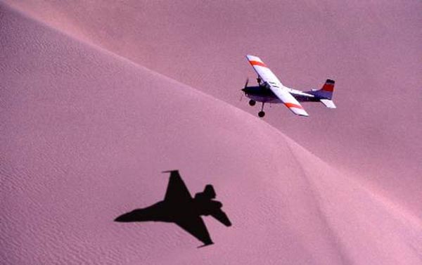 Light aircraft casting shadow of a fighter plane