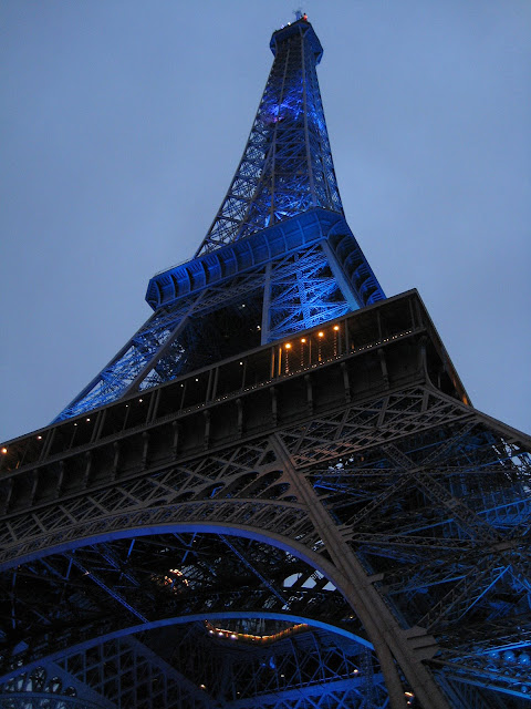 Modře nasvícená Eiffelově věž ve večerním světle.