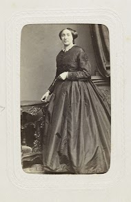 Studioportret van een staande dame in een lange jurk naast een tafel