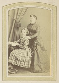 Portret van een meisje in een jurk met Schotse ruit en een vrouw in een jurk bij een tafel met boeken