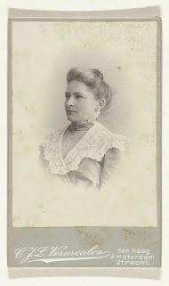 Studioportret van een vrouw in een hooggesloten jurk, afgezet met een kantenkraag