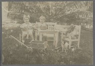 Klaas en Tiny Kleiterp zittend temidden van speelgoed in een tuin in Madjene op Celebes