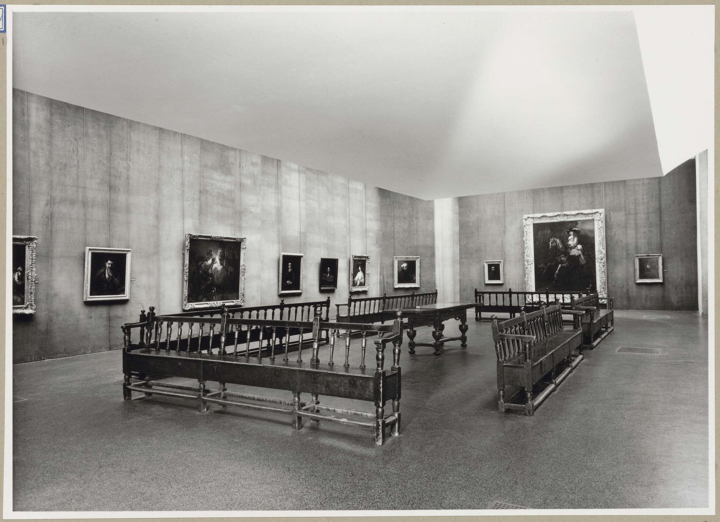 Zaal met tien schilderijen en een tafel te midden van banken