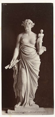 Marmeren beeld van een vrouw met in haar linkerhand een beeld, in haar rechterhand draagt zij een passer en een liniaal.