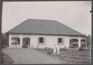 Man en een vrouw poserend in een tuin voor een woonhuis, vermoedelijk op het terrein van een ziekenhuis in Nederlands-Indië